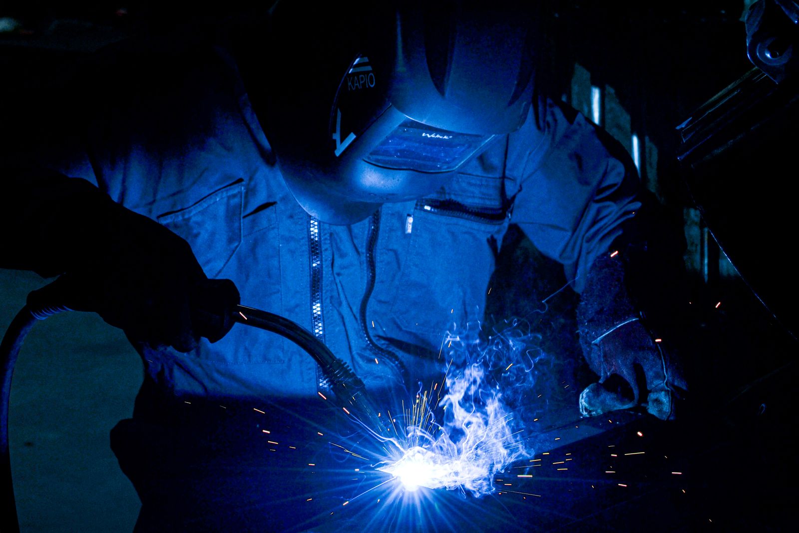 A welder in a protective mask working on steel, with sparks and blue light