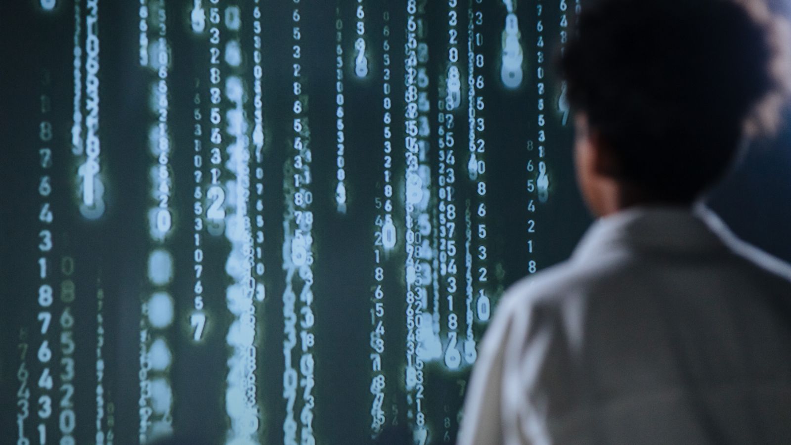 A person in front of a screen of glowing data columns
